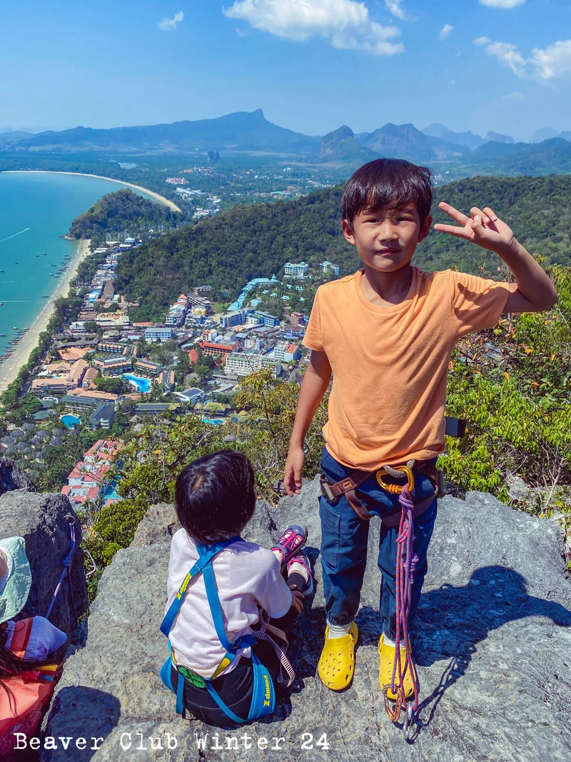 A child wearing a climbing harness at a high viewpoint above a coastal town