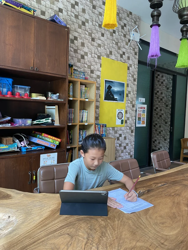 Our son working with a laptop and notebook at the wooden table at home