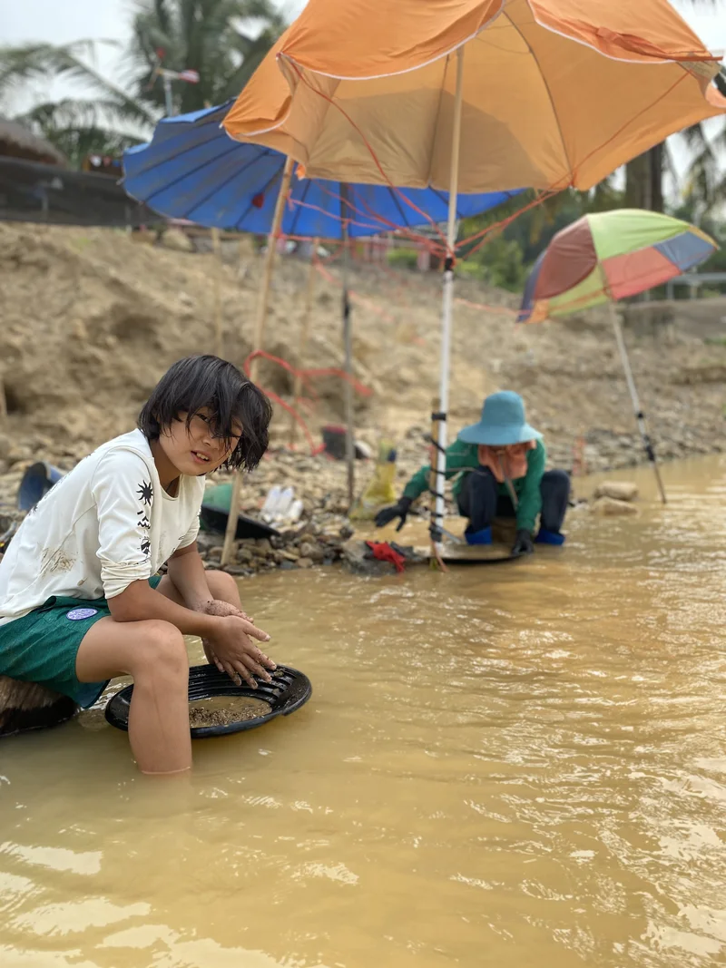 Our son trying gold panning in shallow water under a sun umbrella