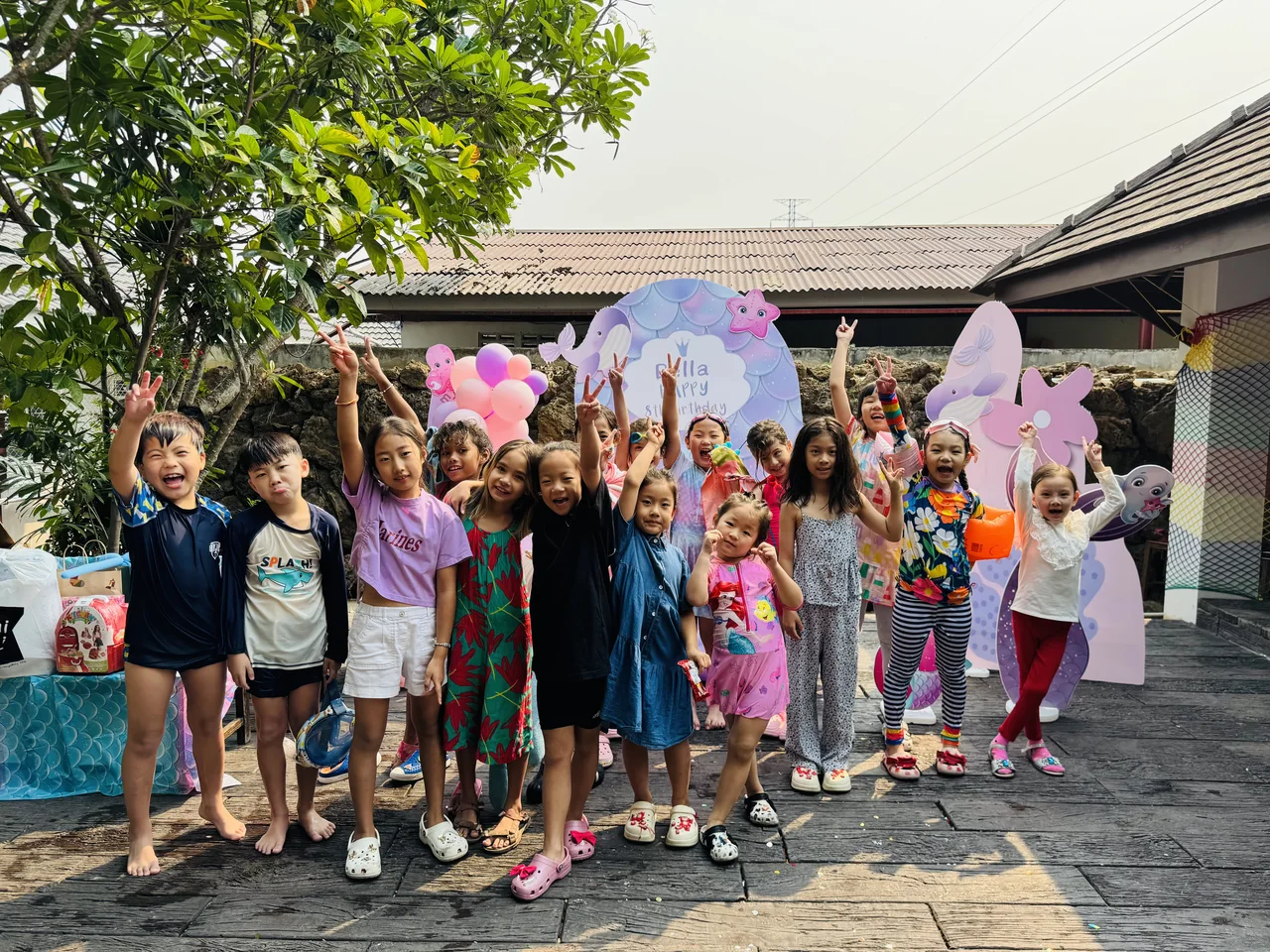 Children raising their hands and smiling beside a colourful birthday backdrop at Beaver Club