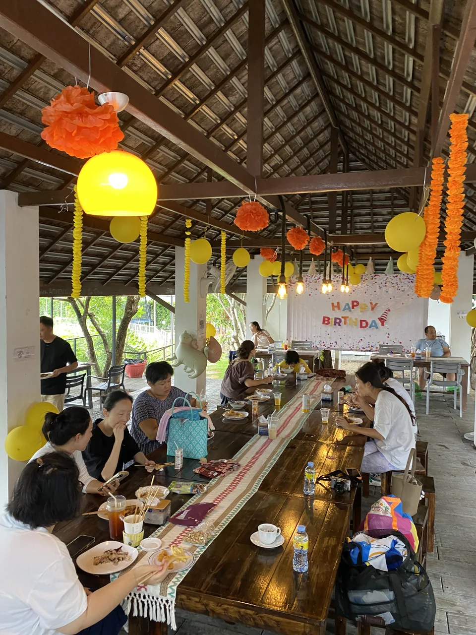 Birthday tables beneath orange and yellow decorations with a birthday backdrop in the pavilion