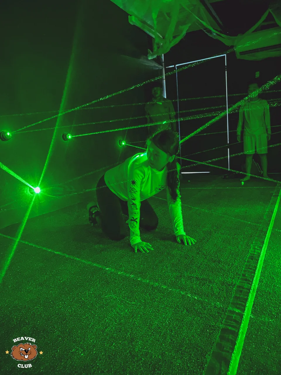 A child crawling beneath green laser beams in the Beaver Club laser room