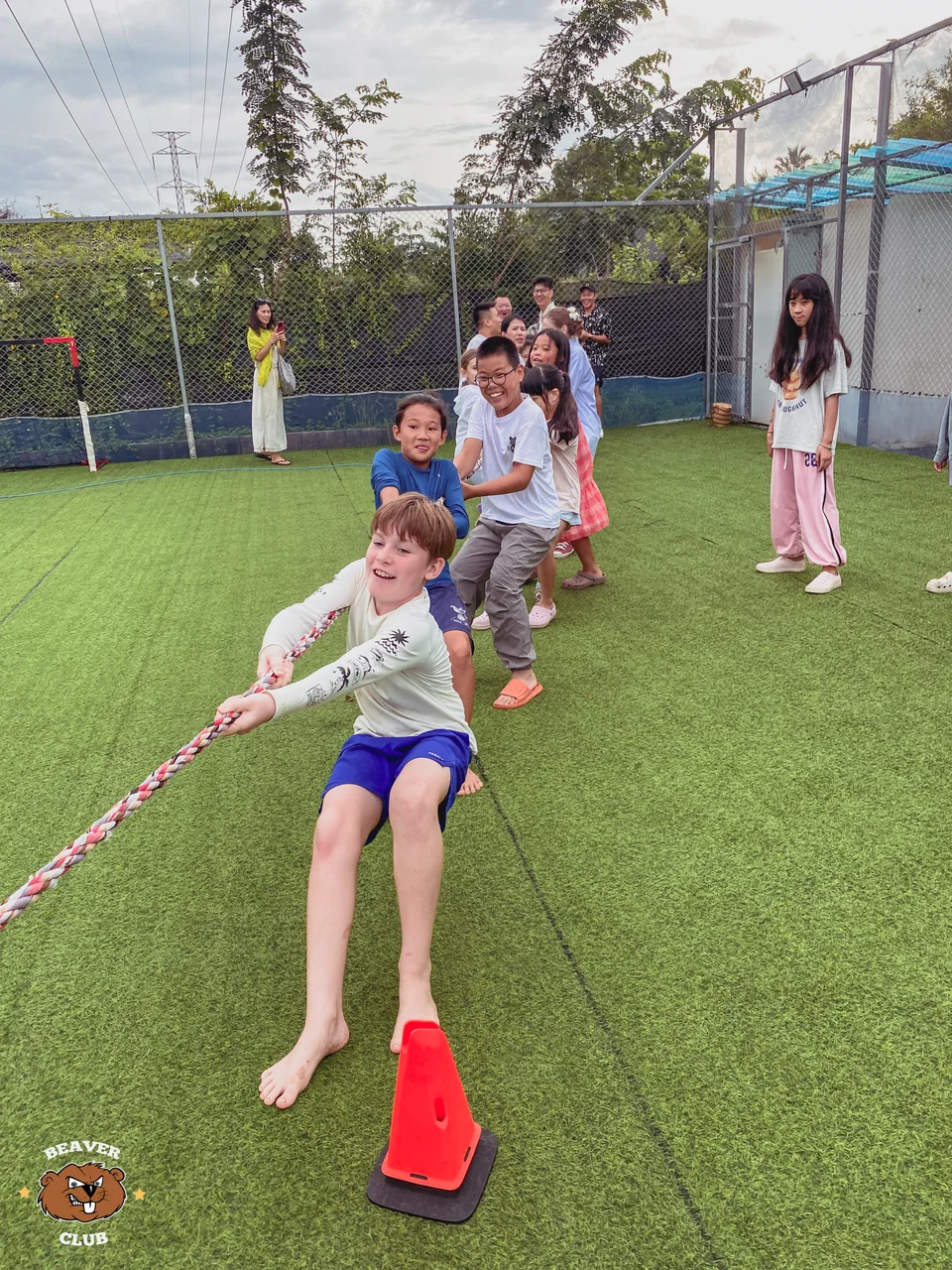 Children leaning back together during a tug-of-war game on the sports field