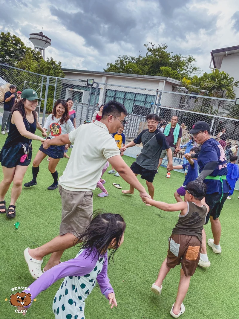 Parents and children holding hands during a group game on the Beaver Club sports field