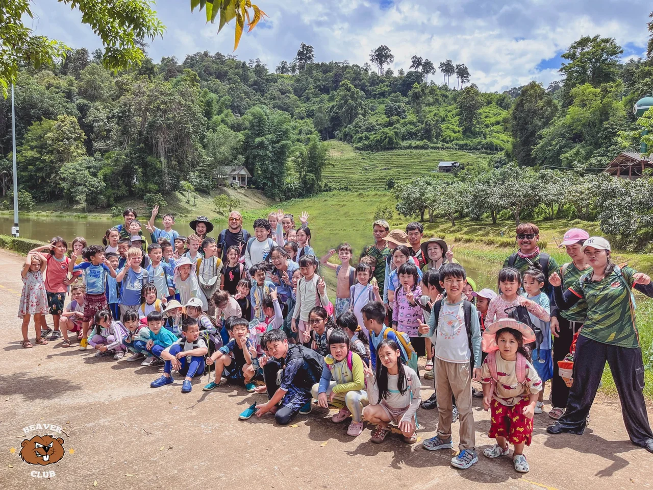 Campers and staff gathered for a group photo beside a lake and wooded hills
