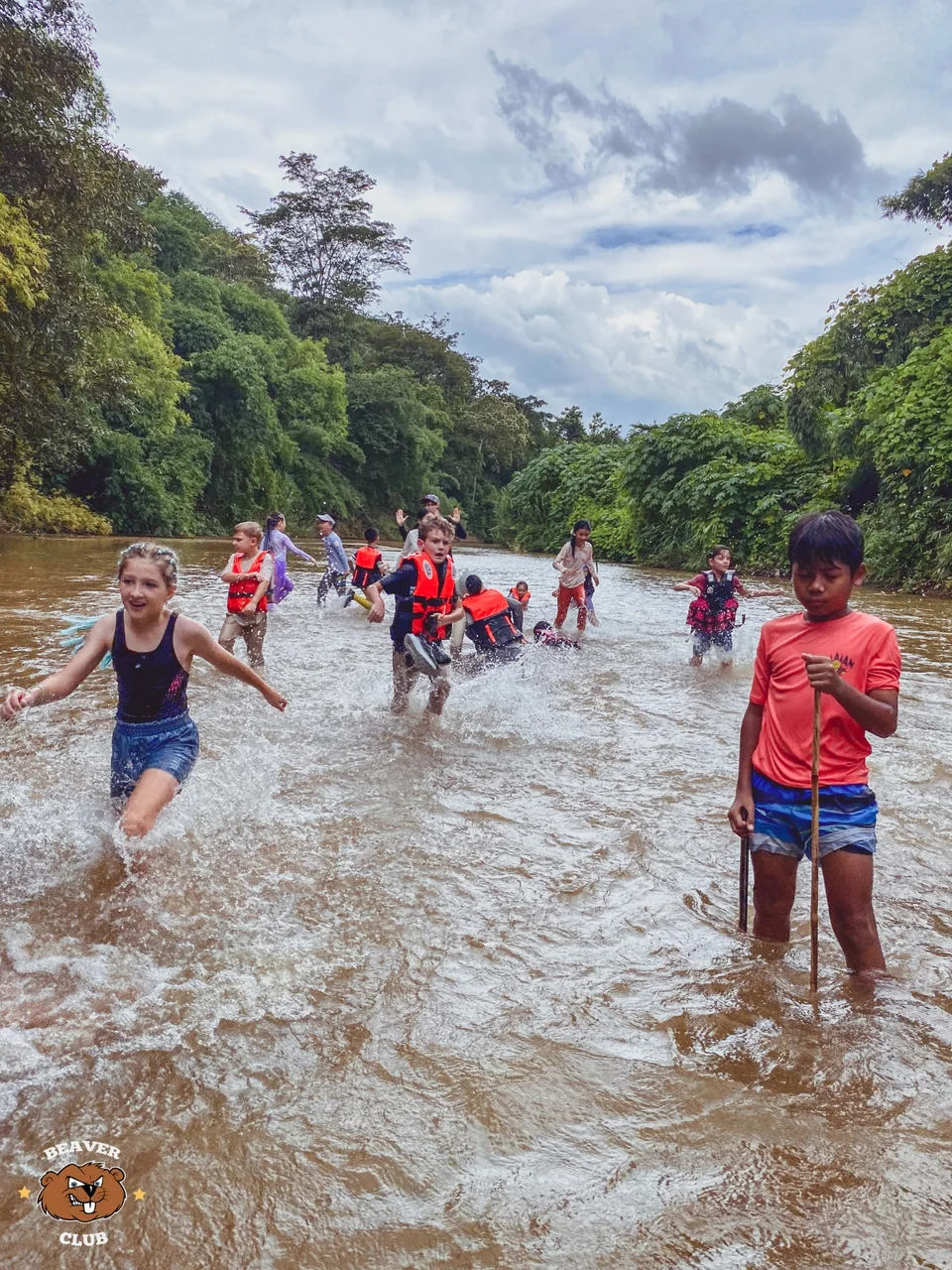 Children wading together through a shallow river surrounded by forest
